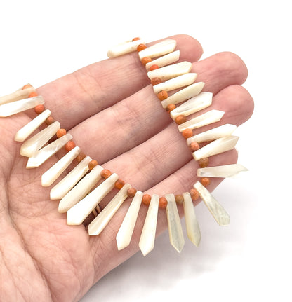 The necklace curved across an open palm, giving a sense of scale: each mother of pearl picket is roughly a finger's width long, with tiny coral beads between them.