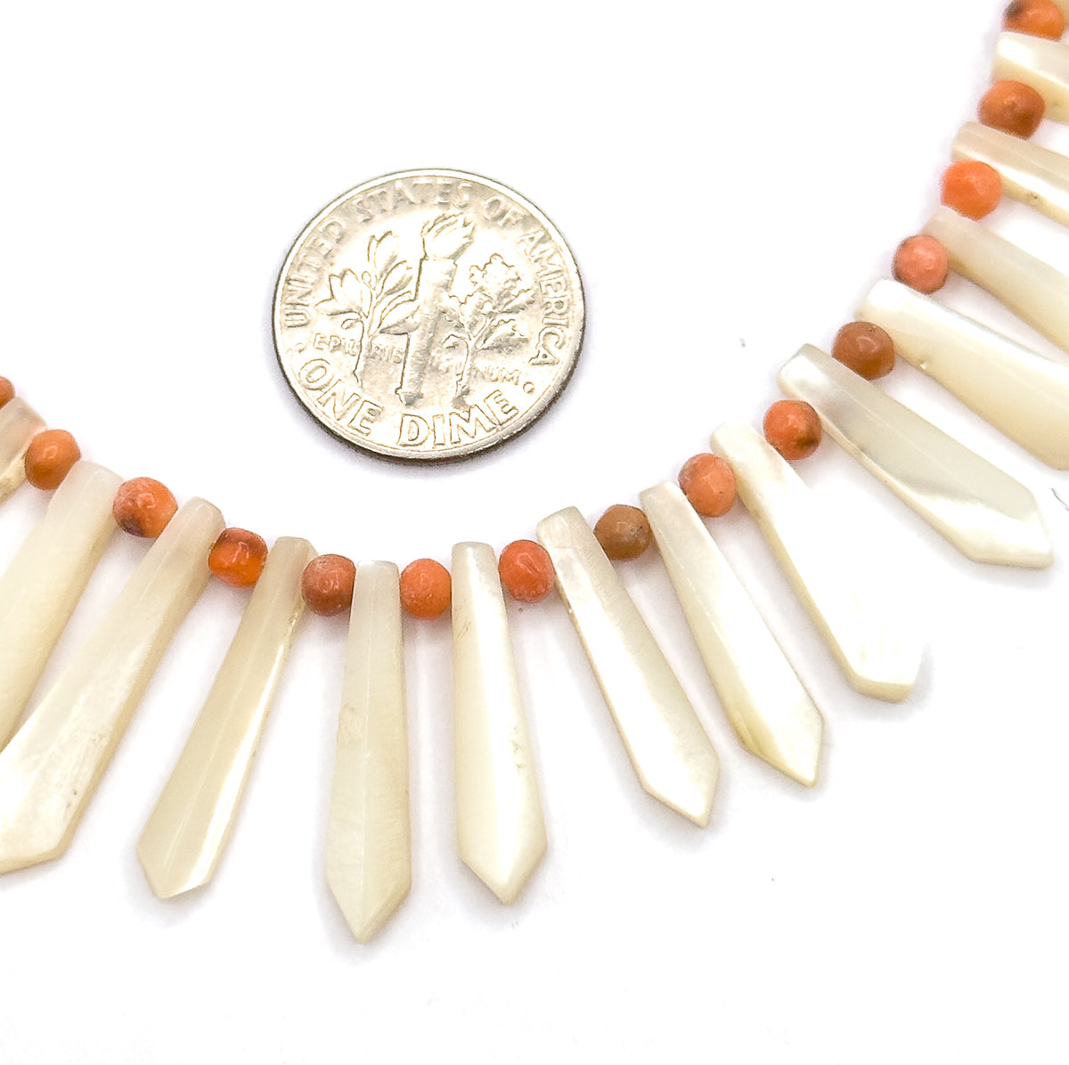 A dime laid beside the necklace for scale, its diameter roughly matching the width of two mother of pearl pickets and the coral beads between them.