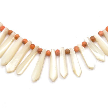 A tight close-up of the centre front, showing the flat facetted faces of the mother of pearl pickets and the round coral beads strung above each gap along the cord.