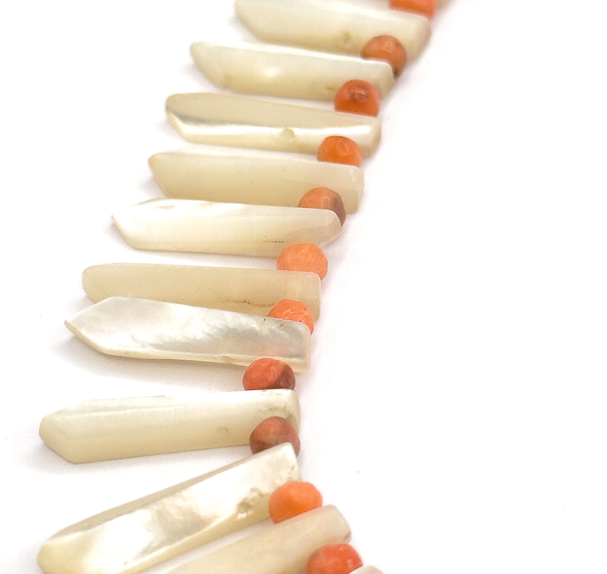 A steep side-on view along the strand, so the pointed tips of the mother of pearl pickets stand out in profile and the coral beads sit in a receding line behind them.