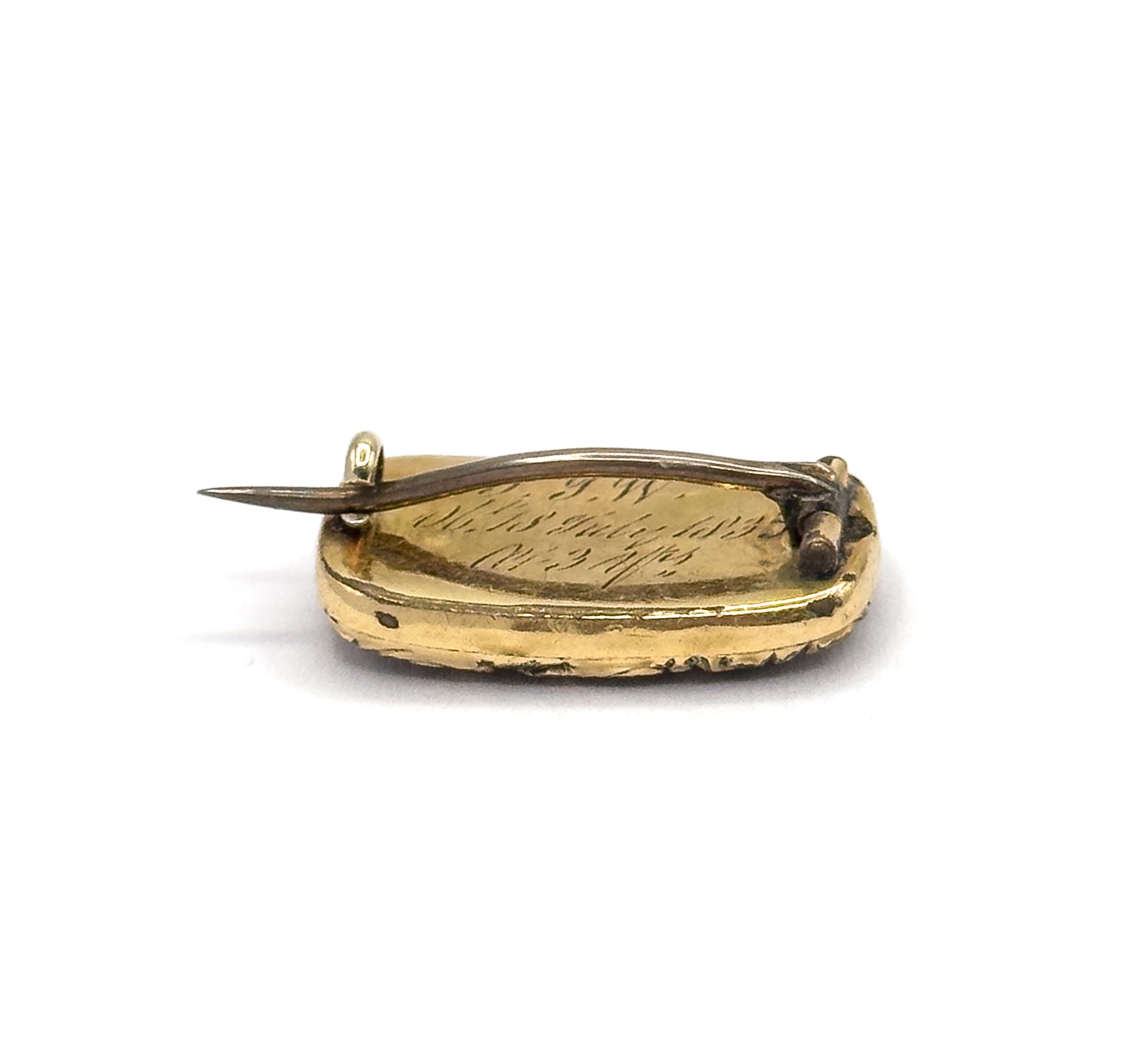 A low edge-on angle showing the brooch's shallow depth, the engraved back curving away, with the pin stem projecting from its hinge at one end and the catch at the other.