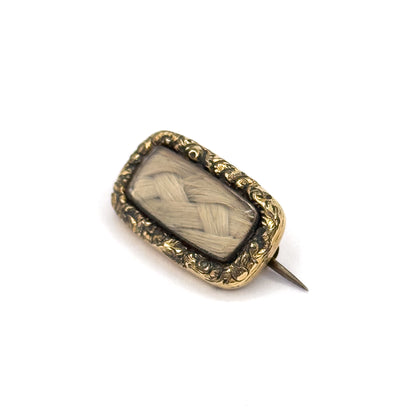 Angled so the frame's shallow side wall shows along one edge, the brooch sits small on white with its open pin stem sweeping out to the lower right and its sharp tip clear of the body.