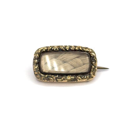 Straight-on face view centred on white, the rectangular hair panel and its scrolling gold plated border squared to the camera, with the pin stem reaching out level to the right.