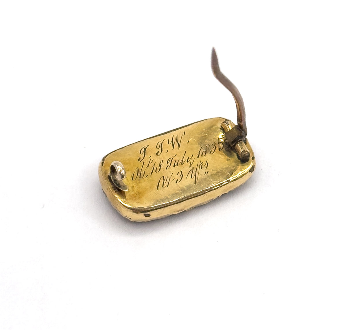 Georgian woven hair mourning brooch shown from the back on white, the rounded rectangular gold plated panel carrying script engraving, with its long pin stem raised above the catch.