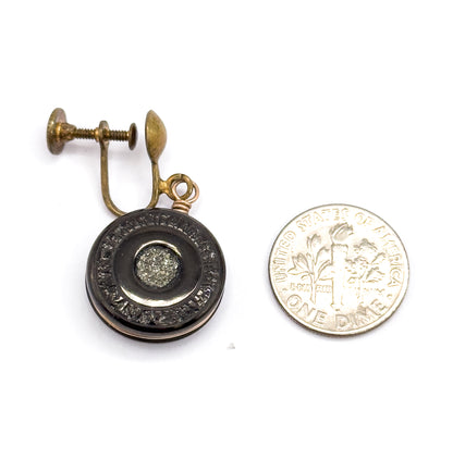 A single earring laid beside a dime for scale, the anthracite disc slightly larger than half the coin, its pyrite centre set in a recessed well below the wire loop and screw back.
