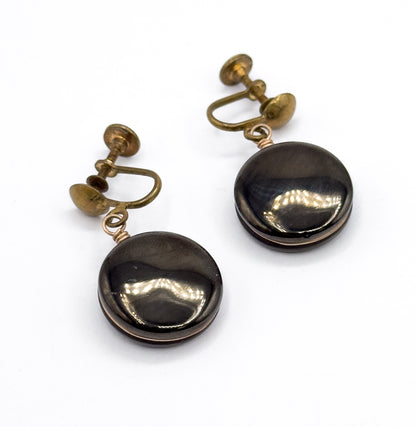 Both earrings angled face-up on white, the round anthracite discs catching a broad highlight across each pyrite centre, with the coiled wire loops and screw-back fittings trailing above.