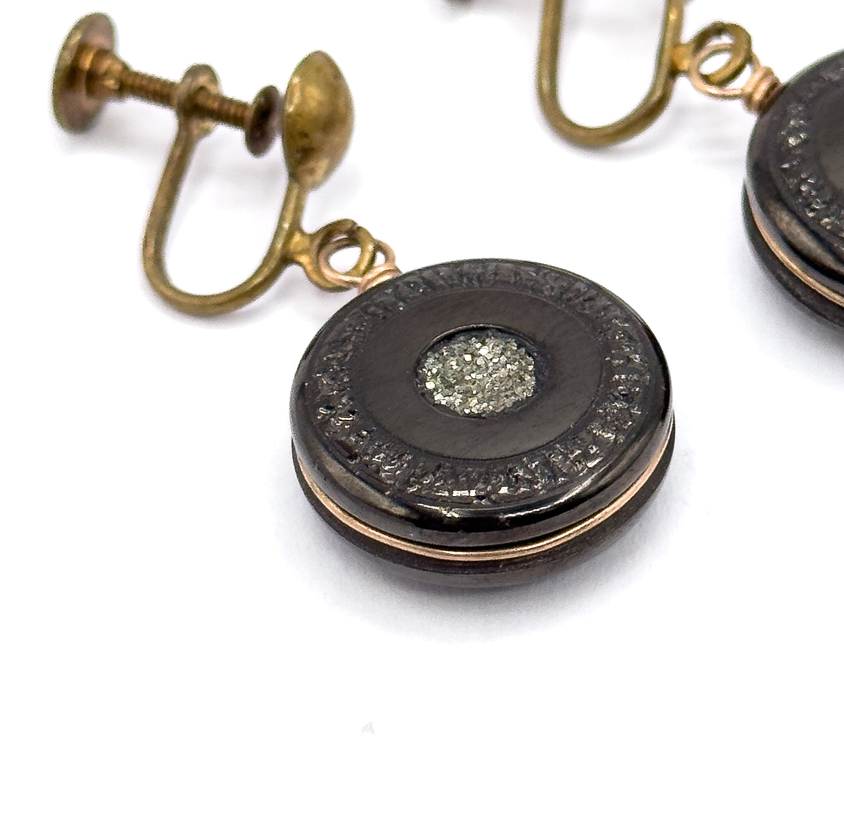 Close macro of one earring filling the frame, revealing the textured border ring encircling the glittering pyrite centre and the loop joining the disc to the screw-back fitting behind.