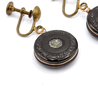 Close macro of one earring filling the frame, revealing the textured border ring encircling the glittering pyrite centre and the loop joining the disc to the screw-back fitting behind.