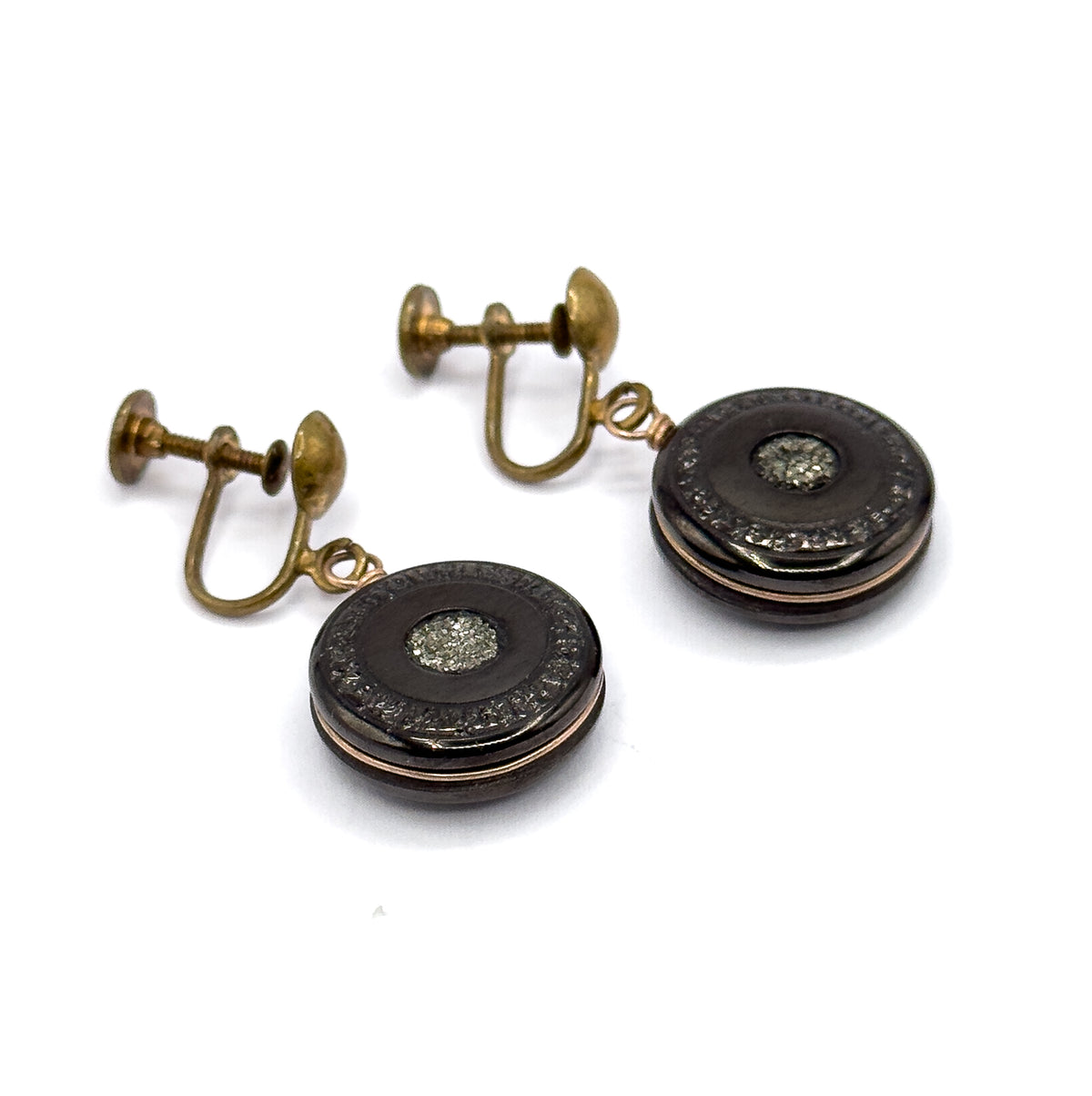 Both earrings laid diagonally on white with the screw backs pointing away at upper left, showing the U-shaped fittings and threaded shafts in full while the two discs sit face-up below.