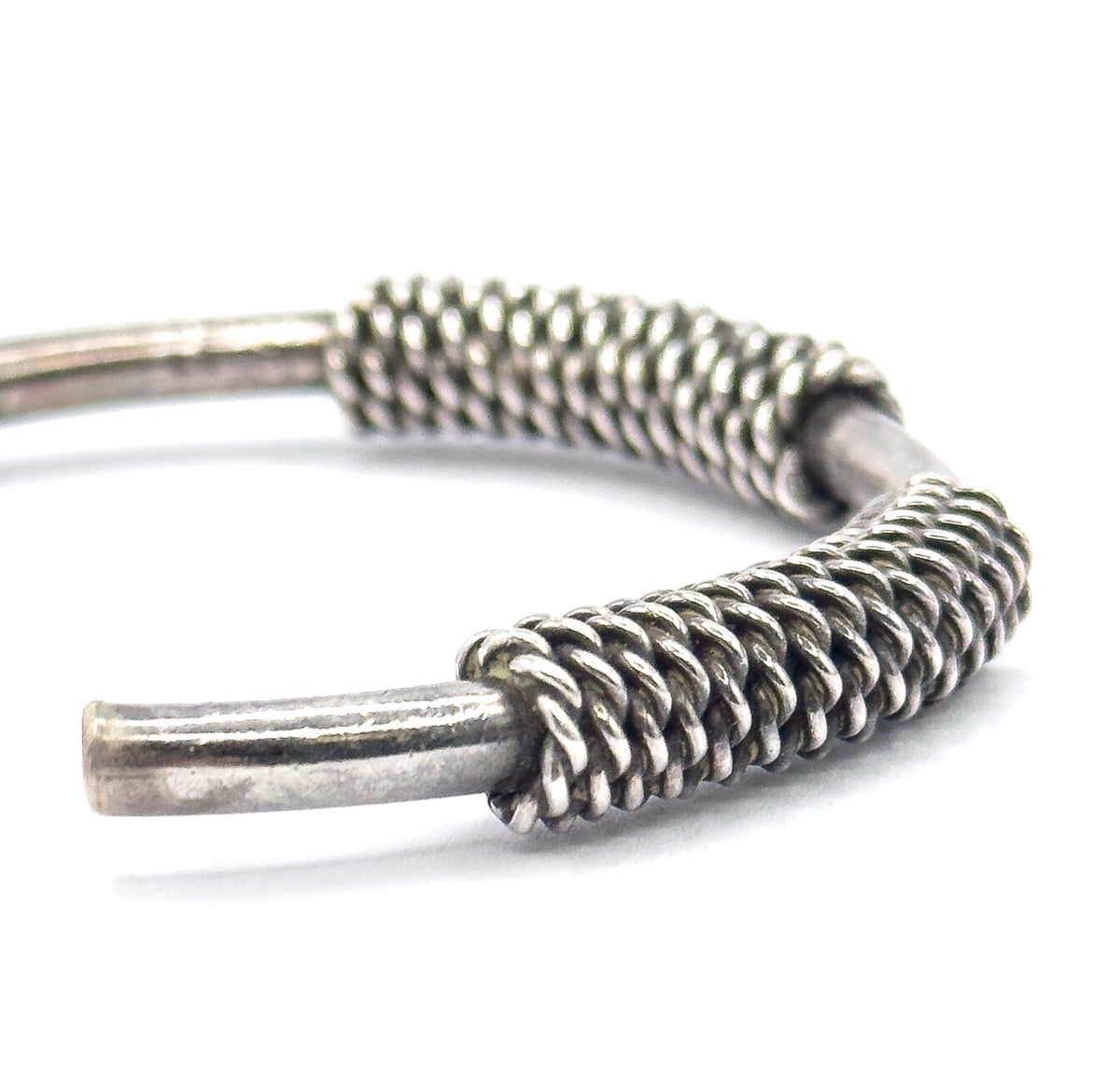Close view of the open terminals, where tightly twisted cable coils wrap the smooth sterling silver rods, patina pooling dark between each turn.