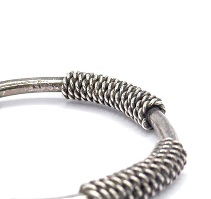 Macro view along the smooth silver rod, where faint stamped marks sit beside a tightly wound coil section that grips the bar and continues around the cuff.