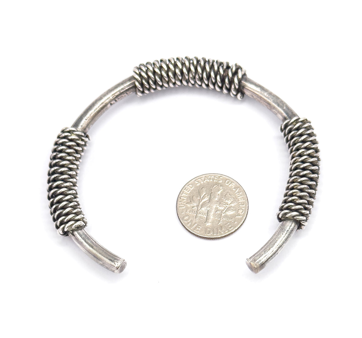 The whole cuff laid flat on white with a dime beside it for scale, showing three coiled cable sections spaced along the curved sterling silver band between its open tapered ends.