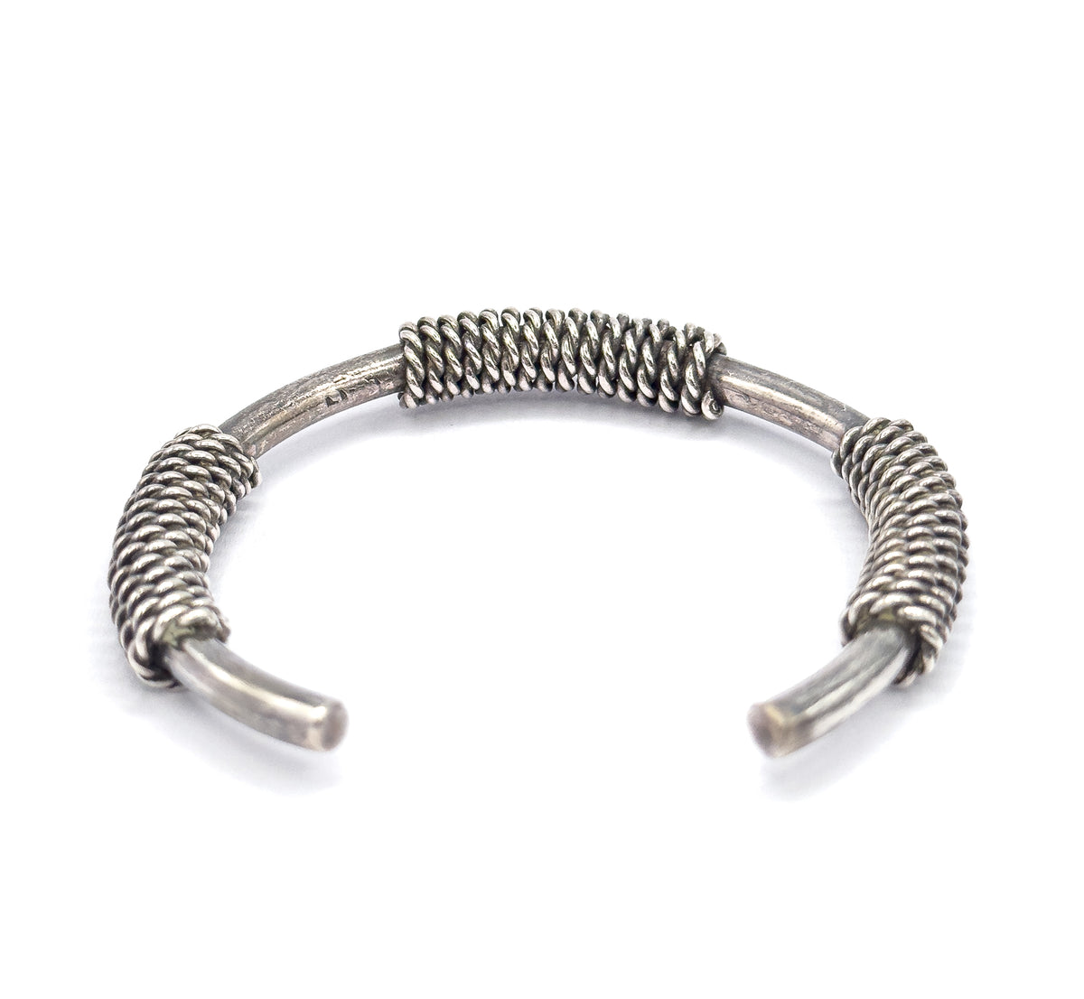 Side-on view of the cuff standing with its opening toward the viewer, so the three coiled sections rise in profile and the tapered terminals curve forward.