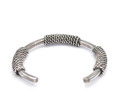 Side-on view of the cuff standing with its opening toward the viewer, so the three coiled sections rise in profile and the tapered terminals curve forward.