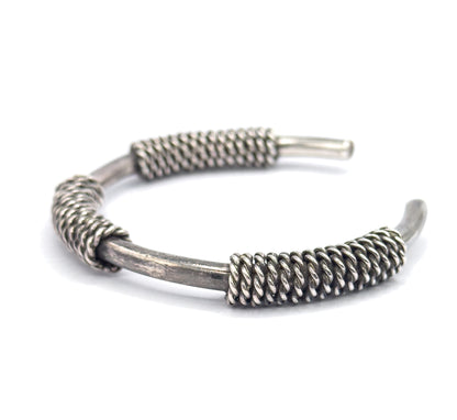 Low angle from the cuff's open side, the band receding toward the back so the twisted coil wraps stand out in relief with dark patina settled between their strands.