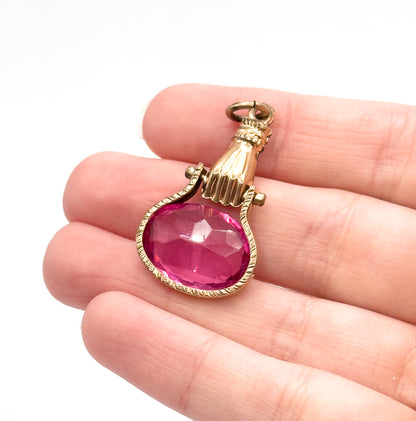 Angled close view on the fingers showing the ruffled cuff, the small pivot lugs at each side of the wrist and the engraved border framing the faceted pink glass.