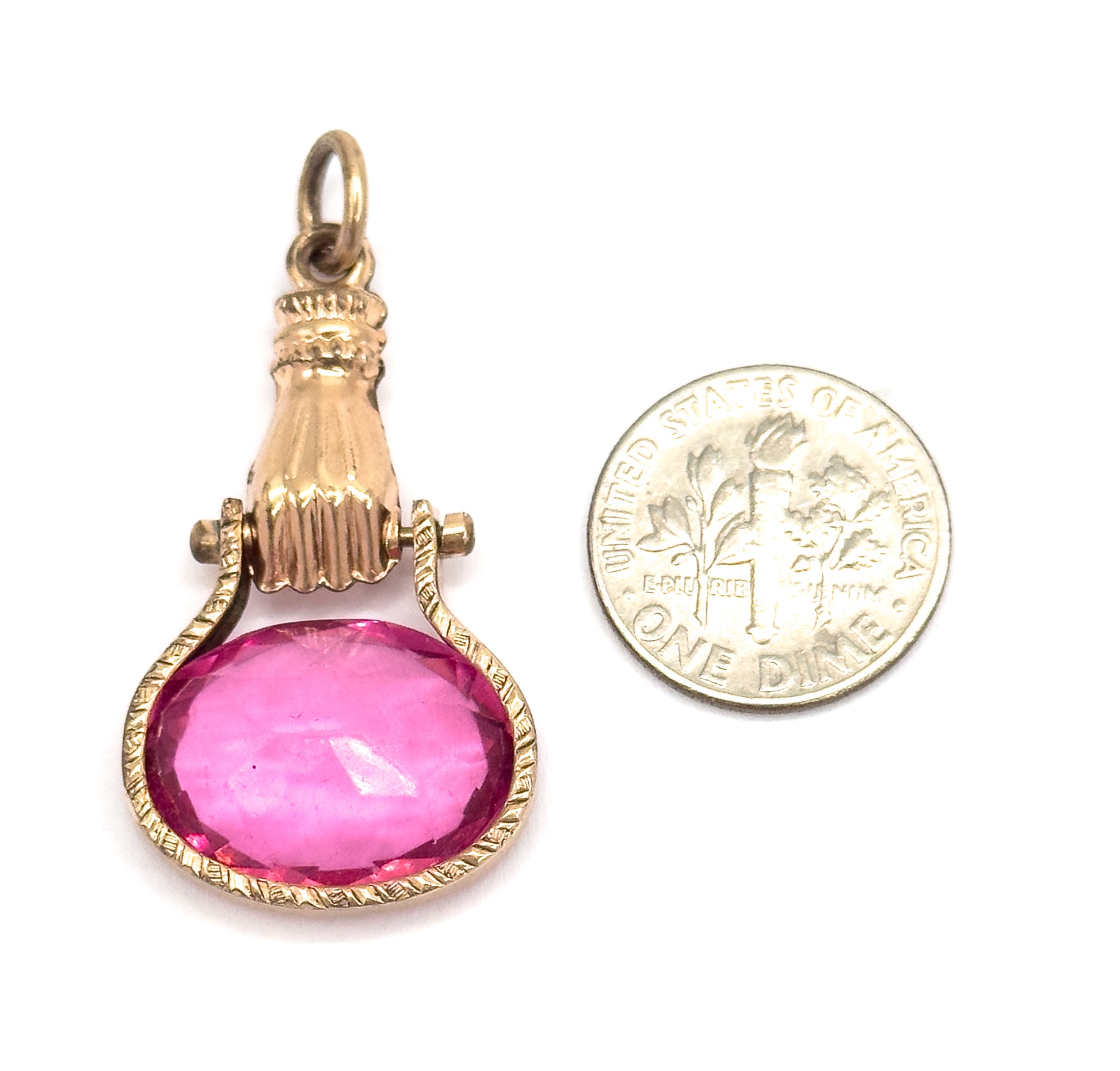 Shown upright beside a dime for scale, the fob's suspension ring, ribbed cuff, pivot lugs and fingers gripping the oval pink glass reading as roughly one and a half coins tall.
