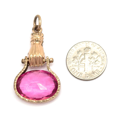 Shown upright beside a dime for scale, the fob's suspension ring, ribbed cuff, pivot lugs and fingers gripping the oval pink glass reading as roughly one and a half coins tall.