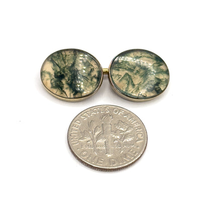 One pair of the oval bezel-set moss agate faces lies above a dime, the two linked stones together spanning roughly the width of the coin.