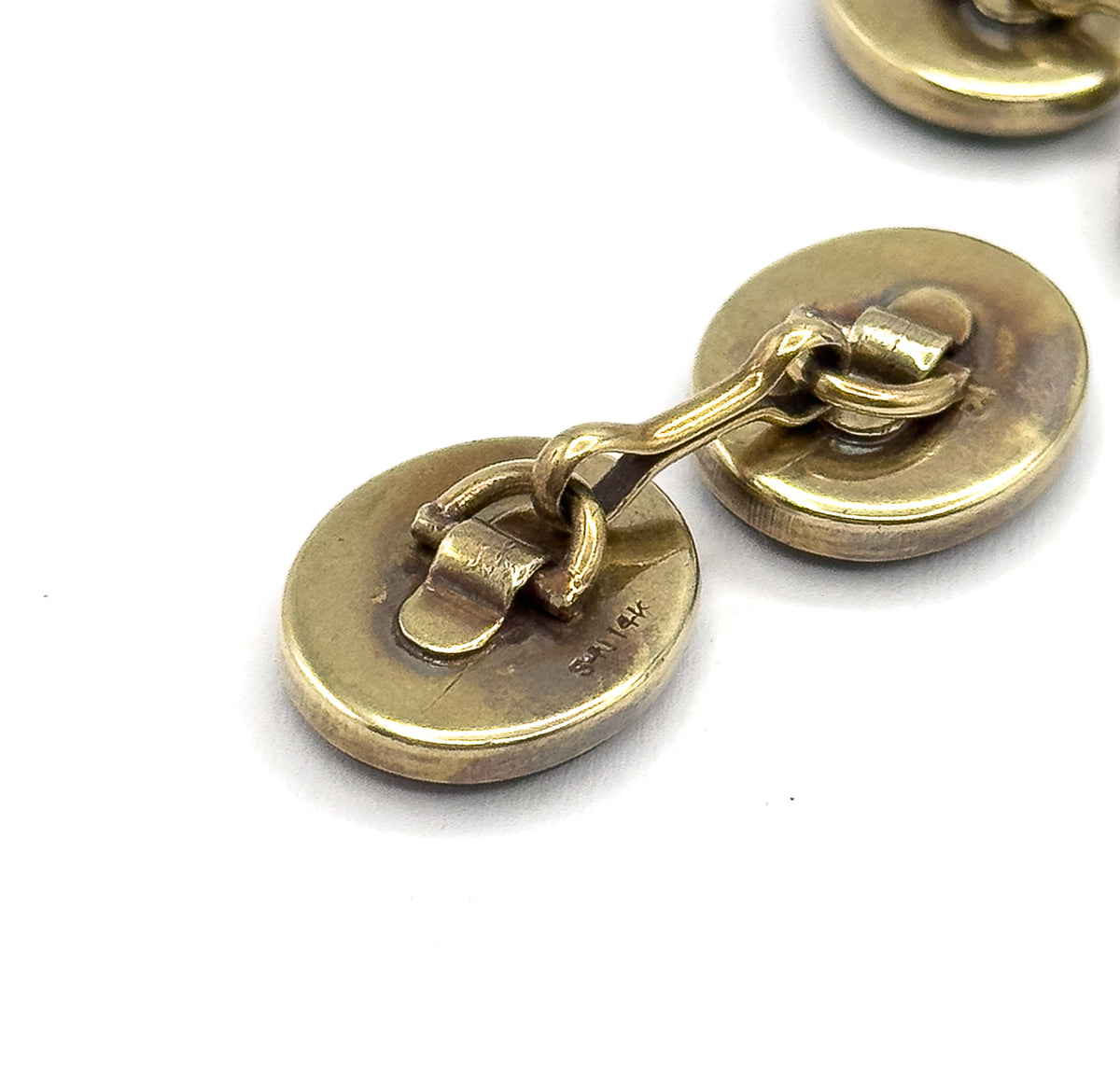 The reverse of one cufflink, its two plain oval yellow gold backs joined by a curved link bar, with a small stamp visible on the lower back.