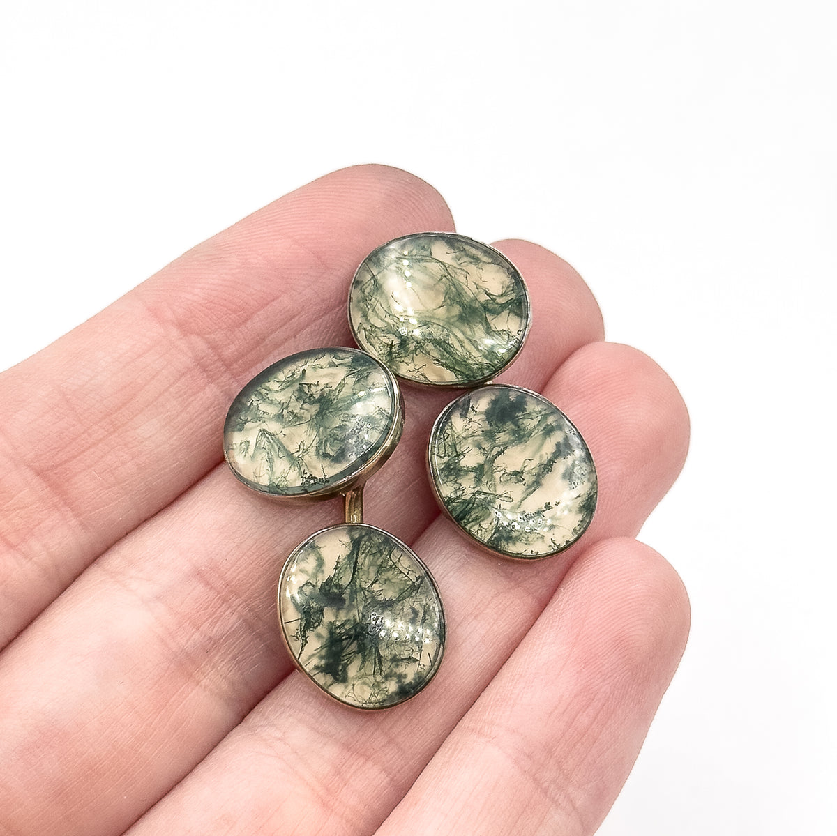Art Deco moss agate cufflinks in 14K yellow gold, their four oval bezel-set stones veined deep green, shown resting across open fingers which give a sense of their small size.