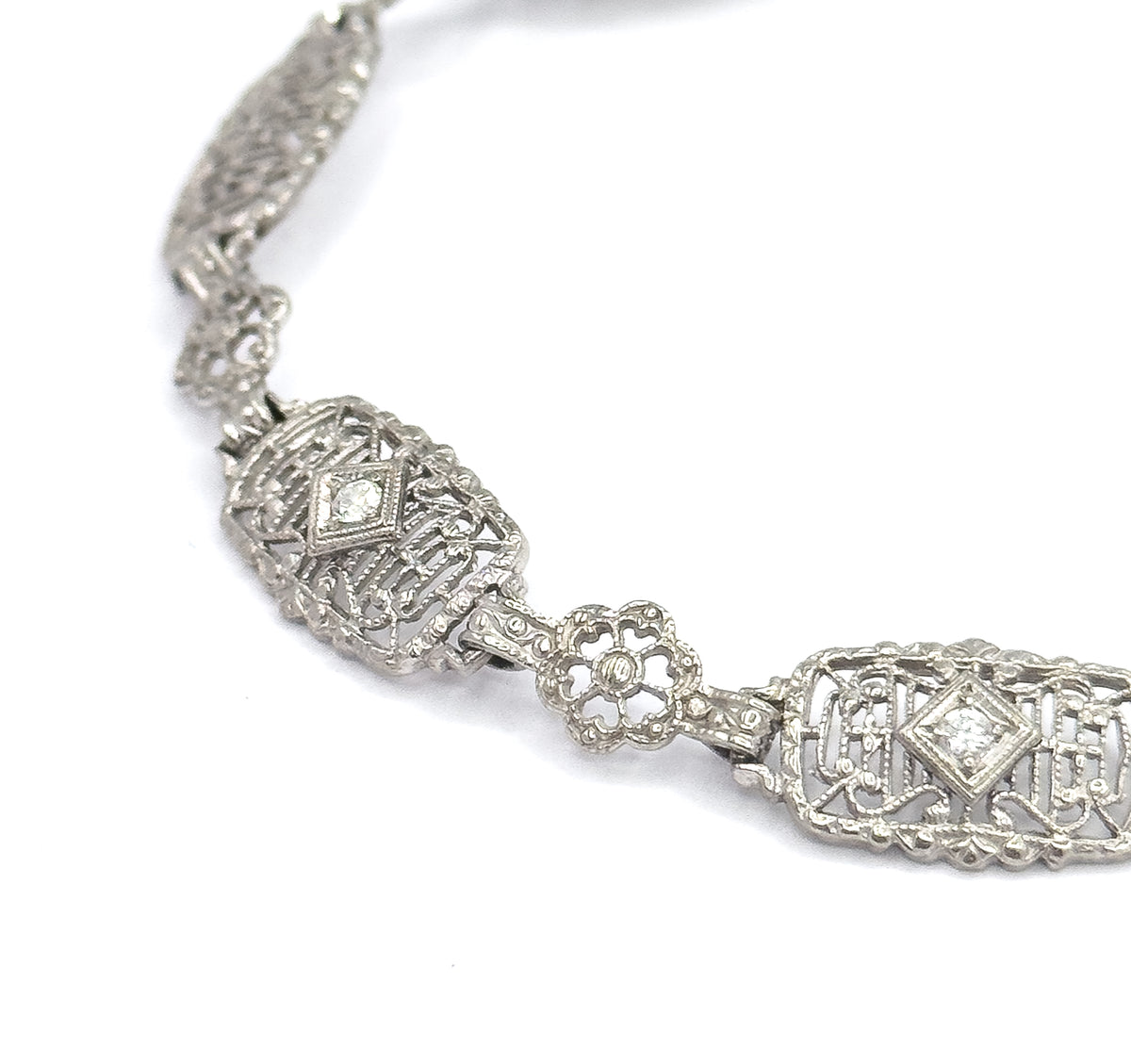 Tighter macro on the same stretch, the diamond-shaped settings holding each prong-set stone and the open centre of the four-petal link now clearly visible against the white ground.