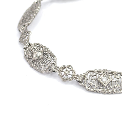 Tighter macro on the same stretch, the diamond-shaped settings holding each prong-set stone and the open centre of the four-petal link now clearly visible against the white ground.