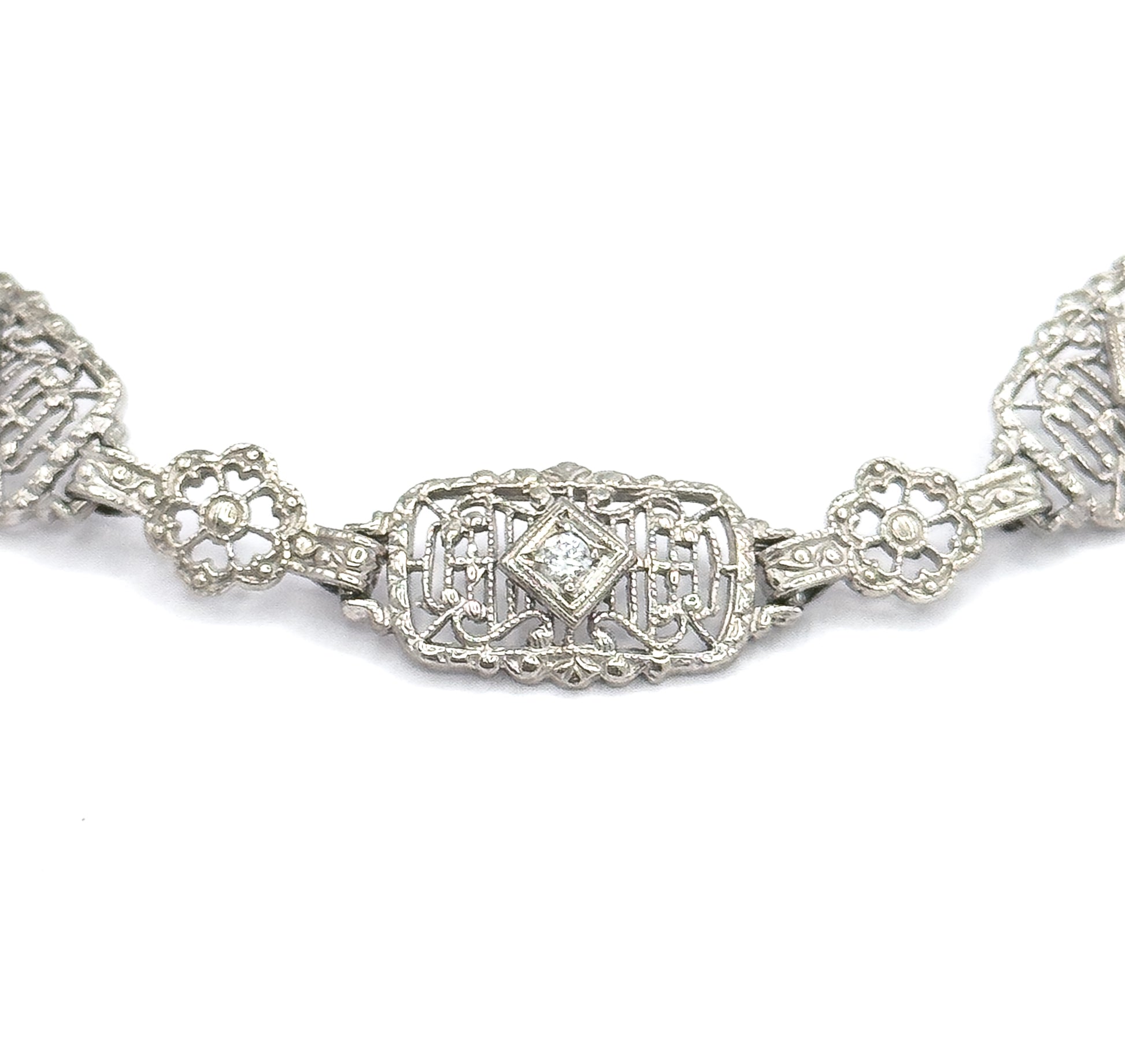 Straight-on macro of a single rectangular filigree link, its centre diamond-shaped setting holding one prong-set stone, with a four-petal floral link on each side and the next links cropped away.