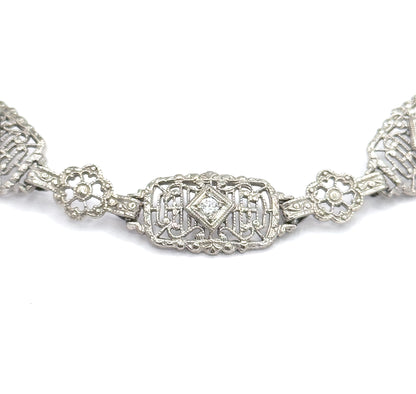 Straight-on macro of a single rectangular filigree link, its centre diamond-shaped setting holding one prong-set stone, with a four-petal floral link on each side and the next links cropped away.