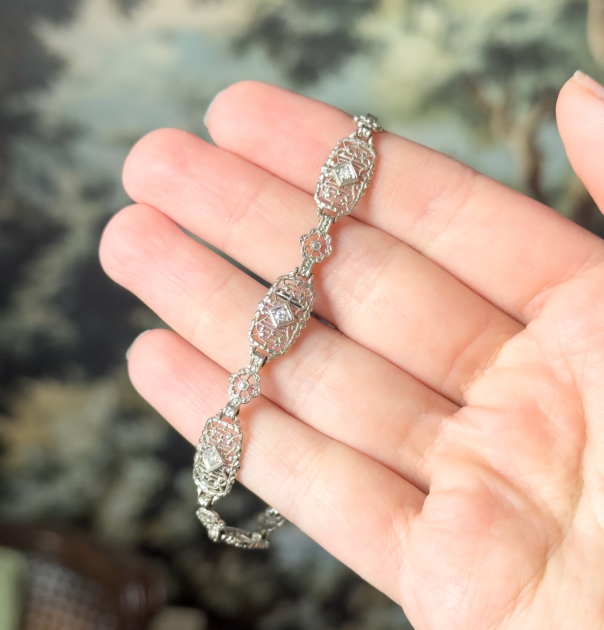 Art Deco diamond filigree bracelet in 14K white gold, shown draped across open fingers so the oval and floral openwork links and prong-set diamonds appear small against the hand.