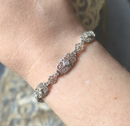 Shown at the wrist, the bracelet curves across the skin so the oval filigree link with its prong-set diamond sits centre, flanked by small floral links and further diamond-set links.