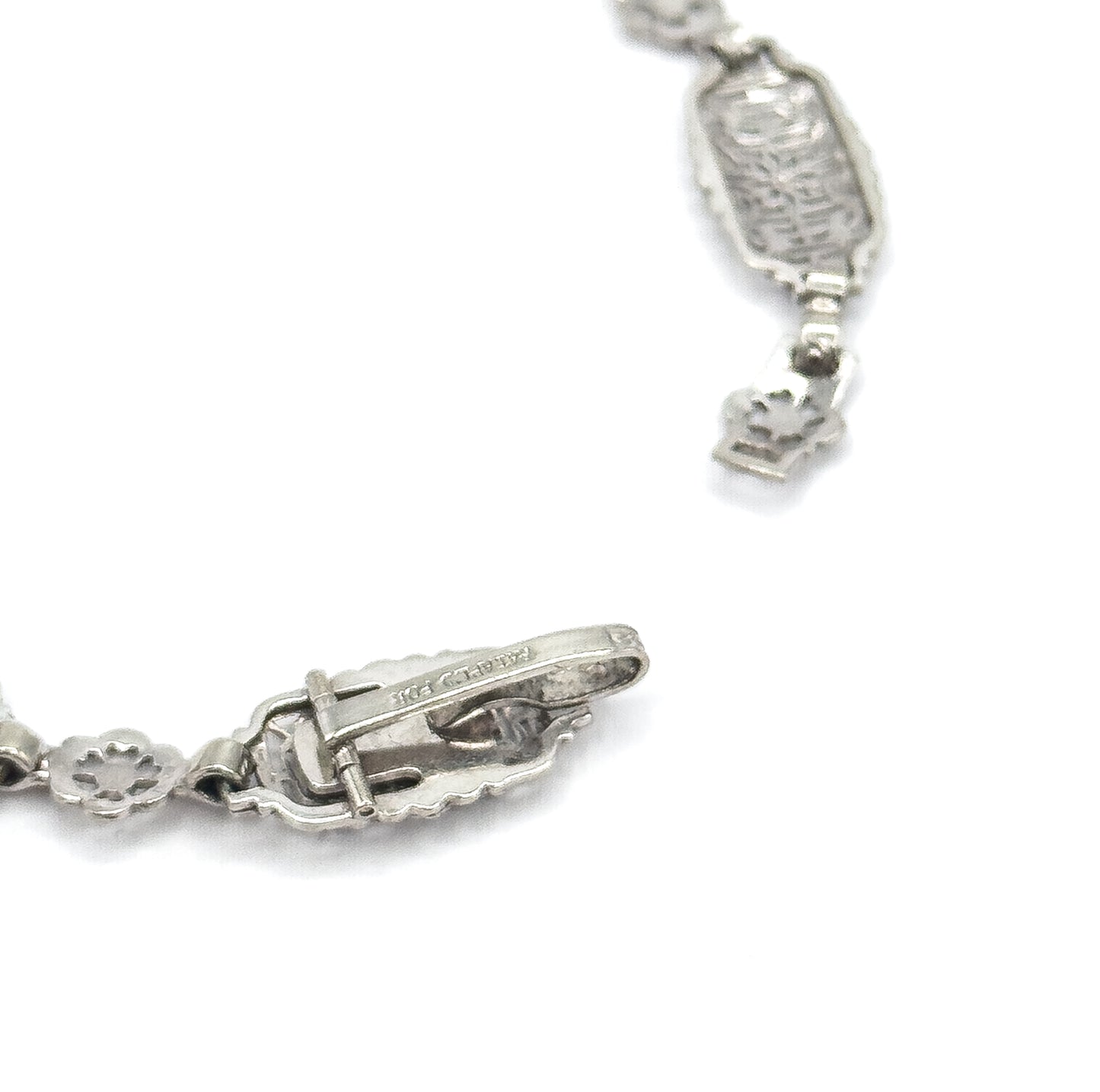 Close view of the reverse, showing the underside of the clasp with its tongue and slot mechanism and stamped mark, alongside the backs of the rectangular and floral links.