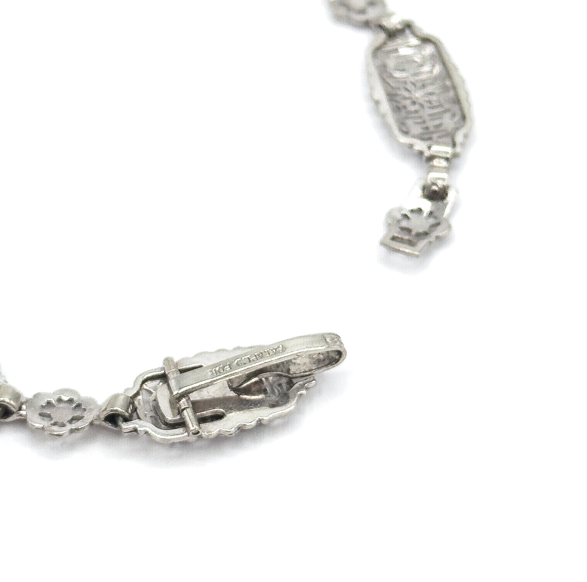 Close view of the reverse, showing the underside of the clasp with its tongue and slot mechanism and stamped mark, alongside the backs of the rectangular and floral links.