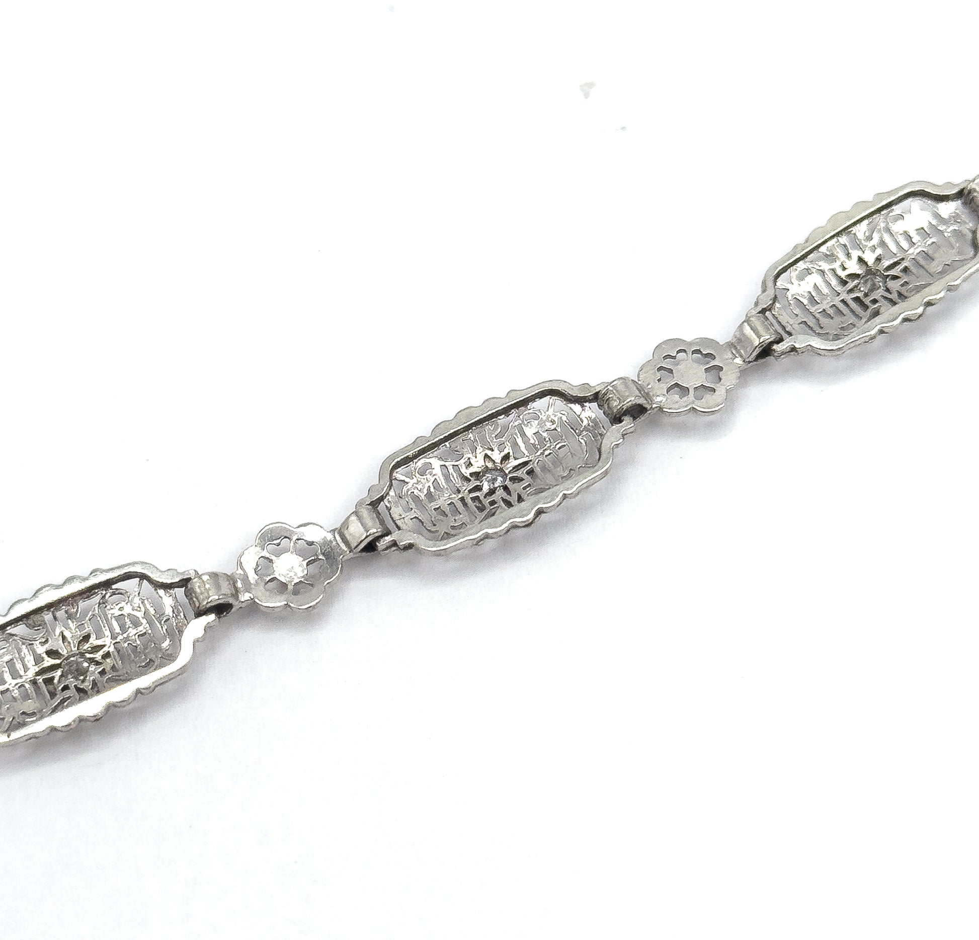 Angled close-up along a section of the chain, showing two oval filigree links each with a prong-set diamond joined by a small pierced floral link between them.