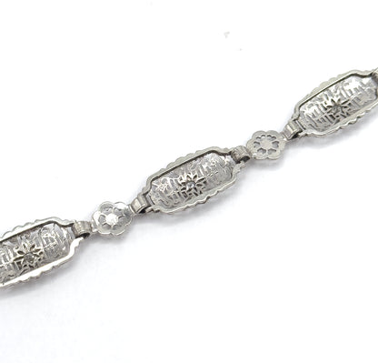 Angled close-up along a section of the chain, showing two oval filigree links each with a prong-set diamond joined by a small pierced floral link between them.