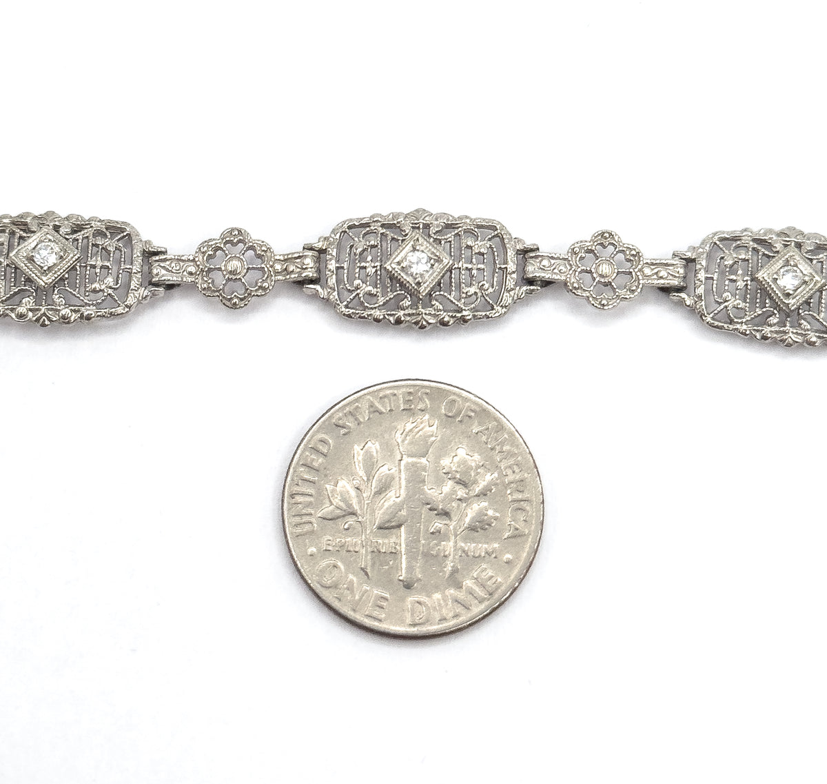 A dime laid below the bracelet gives scale, showing the rectangular filigree links with their prong-set diamonds only slightly wider than the coin's edge.