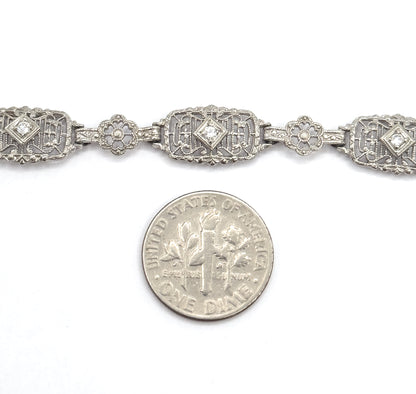 A dime laid below the bracelet gives scale, showing the rectangular filigree links with their prong-set diamonds only slightly wider than the coin's edge.