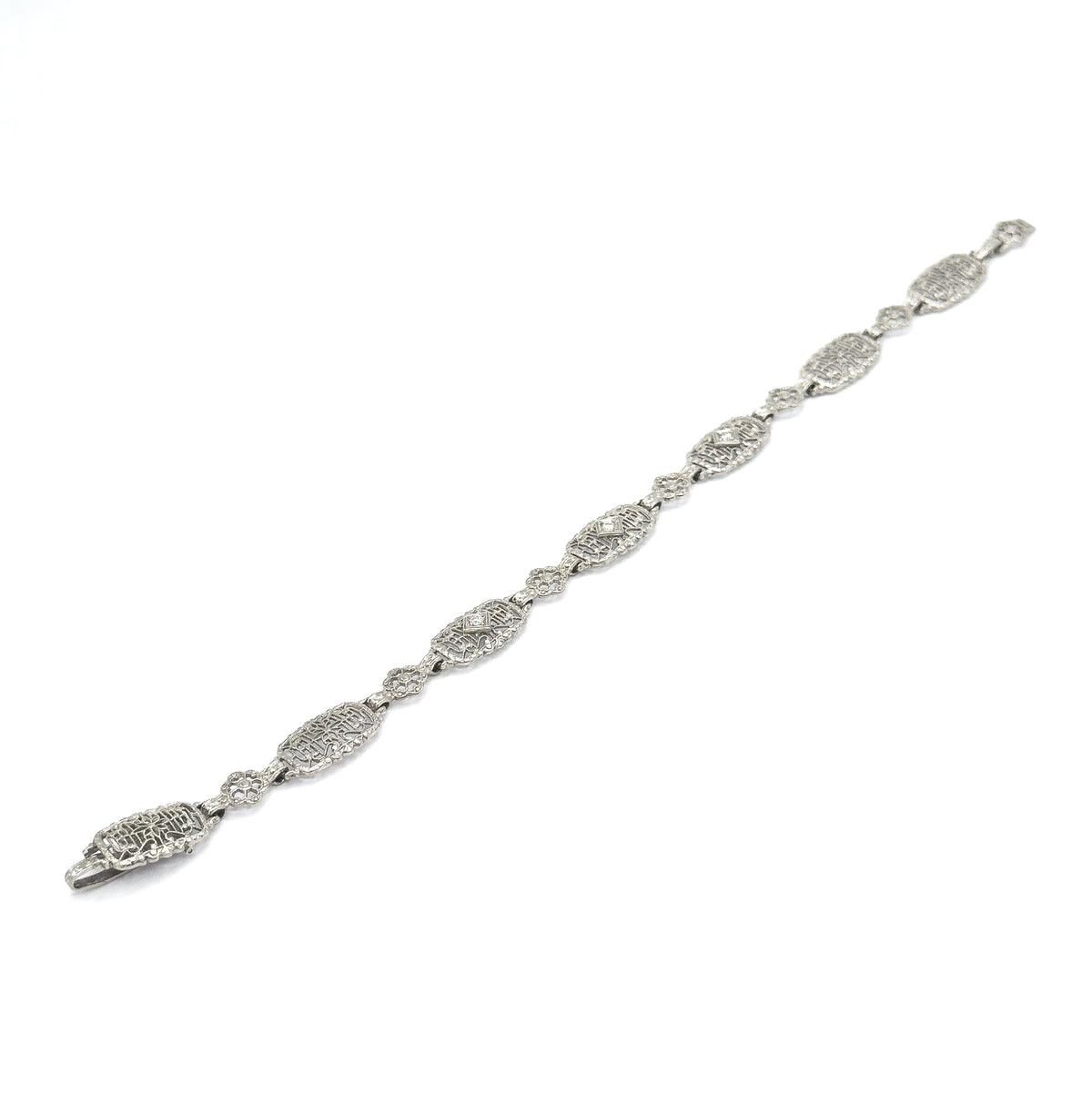 The whole bracelet laid out flat and stretched diagonally across a white background, showing its full length from clasp to end with the alternating oval and floral filigree links.
