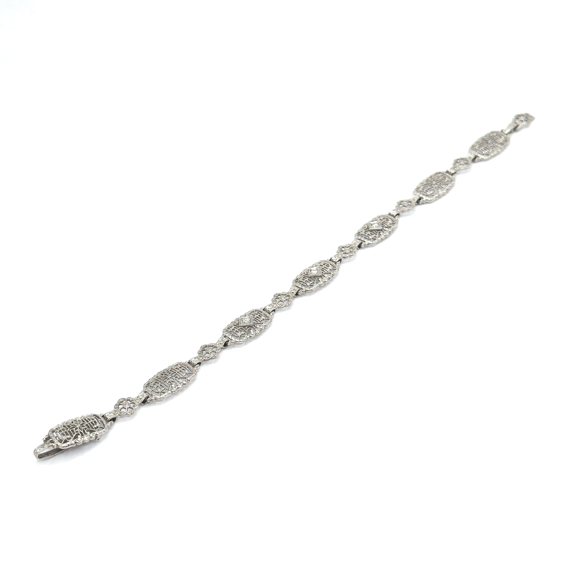 The whole bracelet laid out flat and stretched diagonally across a white background, showing its full length from clasp to end with the alternating oval and floral filigree links.