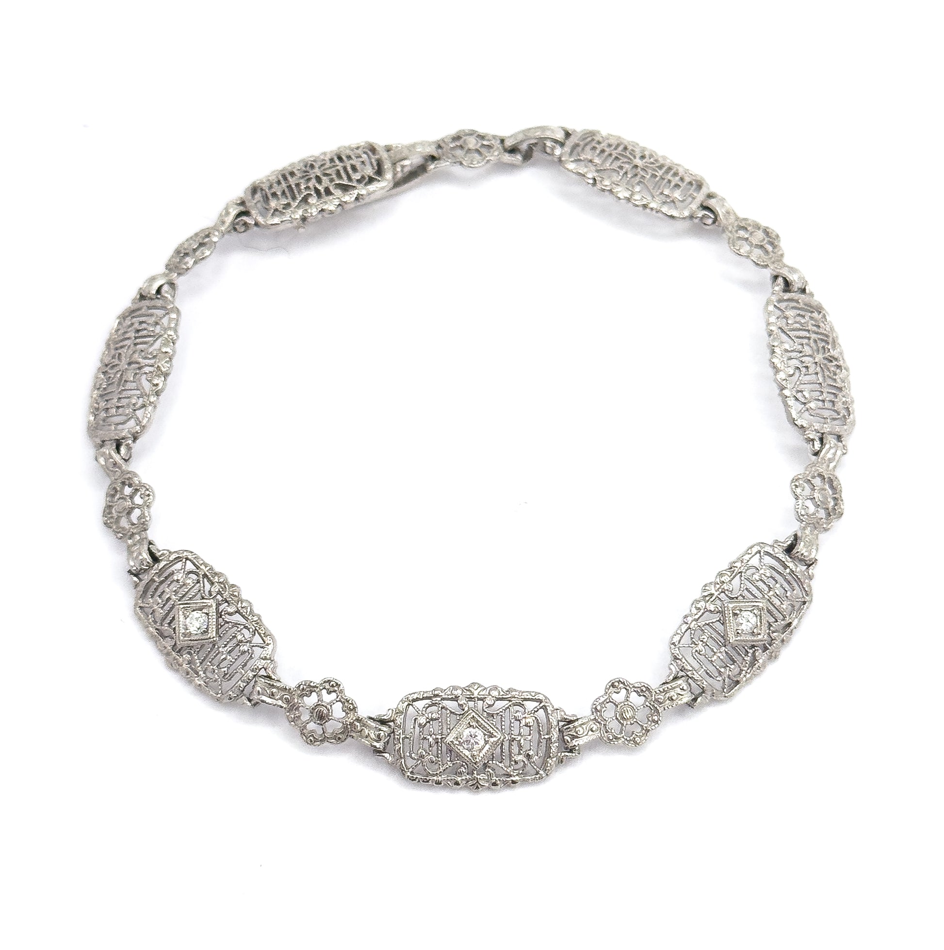 The bracelet curved into a full circle on white, clasp joined at the top, so all the oval filigree links and small floral links can be counted around the loop.