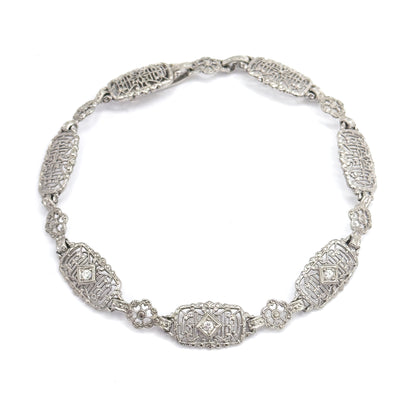 The bracelet curved into a full circle on white, clasp joined at the top, so all the oval filigree links and small floral links can be counted around the loop.