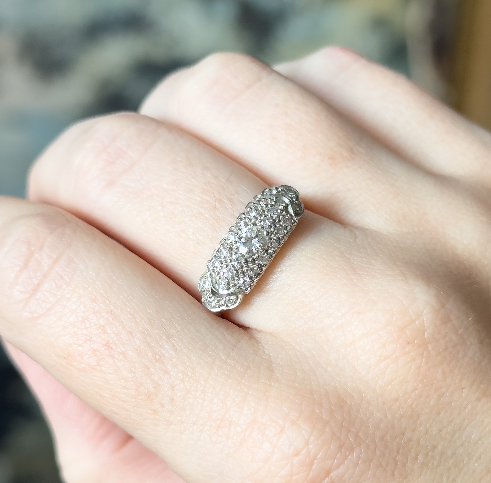 Angled close view on the finger, the domed pavé face turned to catch the light, with the hand giving a sense of the ring's compact scale across the finger.