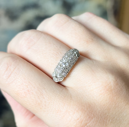 Angled close view on the finger, the domed pavé face turned to catch the light, with the hand giving a sense of the ring's compact scale across the finger.