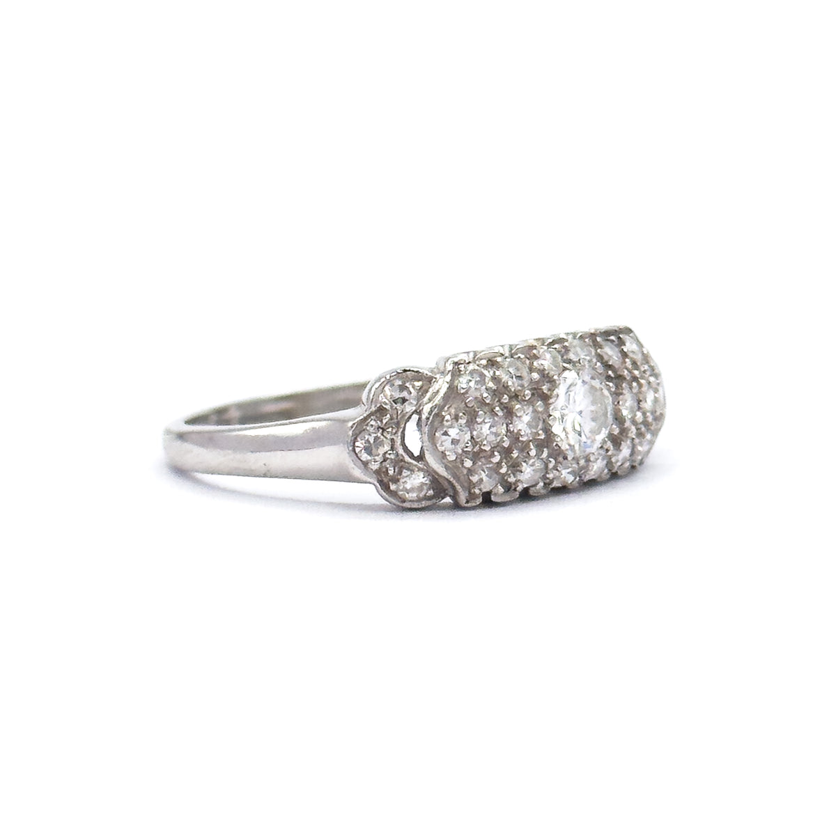 Side profile off the hand against white, the platinum shank rising to scalloped shoulders and the low-domed pavé head, its diamonds seen edge-on in rows.