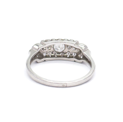 Rear view against white with the shank curving toward the viewer, the underside of the head open so the backs of the centre stone and surrounding pavé show between the scalloped edges.