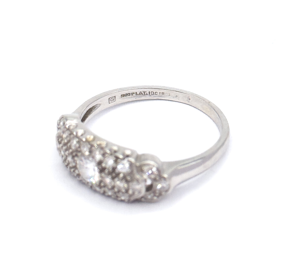 Angled three-quarter view against white with the ring tipped forward, bringing the stamped markings inside the platinum shank into view above the domed pavé head and its centre diamond.