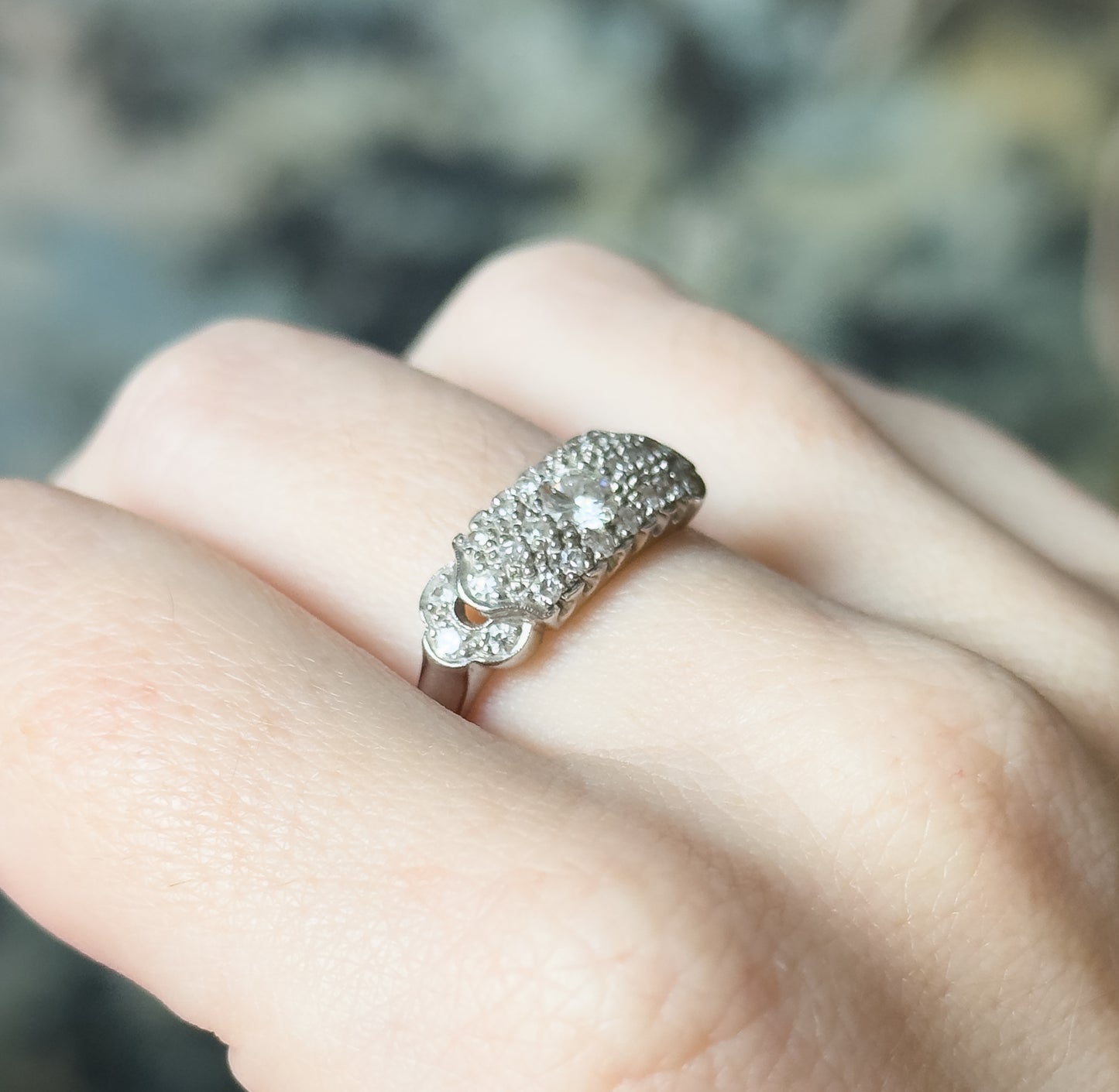A mid-century diamond pavé ring in platinum, shown on a finger, its domed top set with a central diamond framed by rows of smaller stones above smooth shoulders and a polished shank.