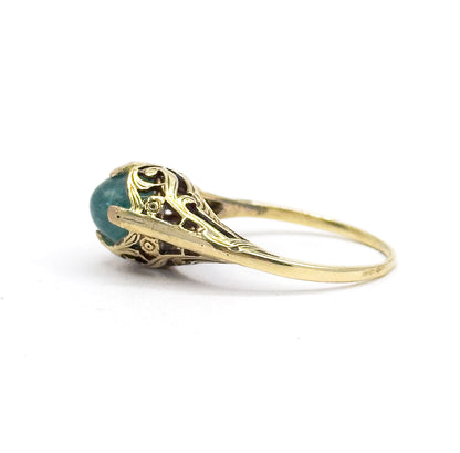 Side view with the shank sweeping away to the right, bringing into focus the tiny engraved flower on the lower gallery wall beside the greenish blue cabochon in its prongs.
