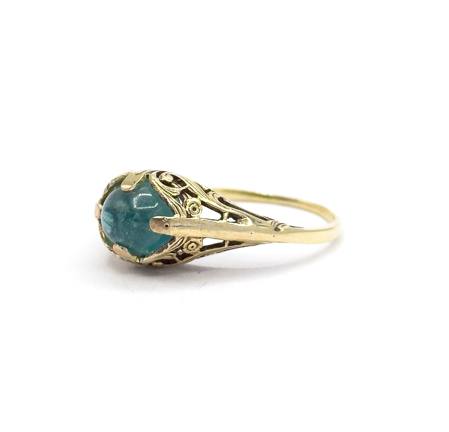 Angled three-quarter view from slightly above, the oval greenish blue cabochon showing its full domed face between four prongs while the pierced fern shoulders taper into the slim split shank.