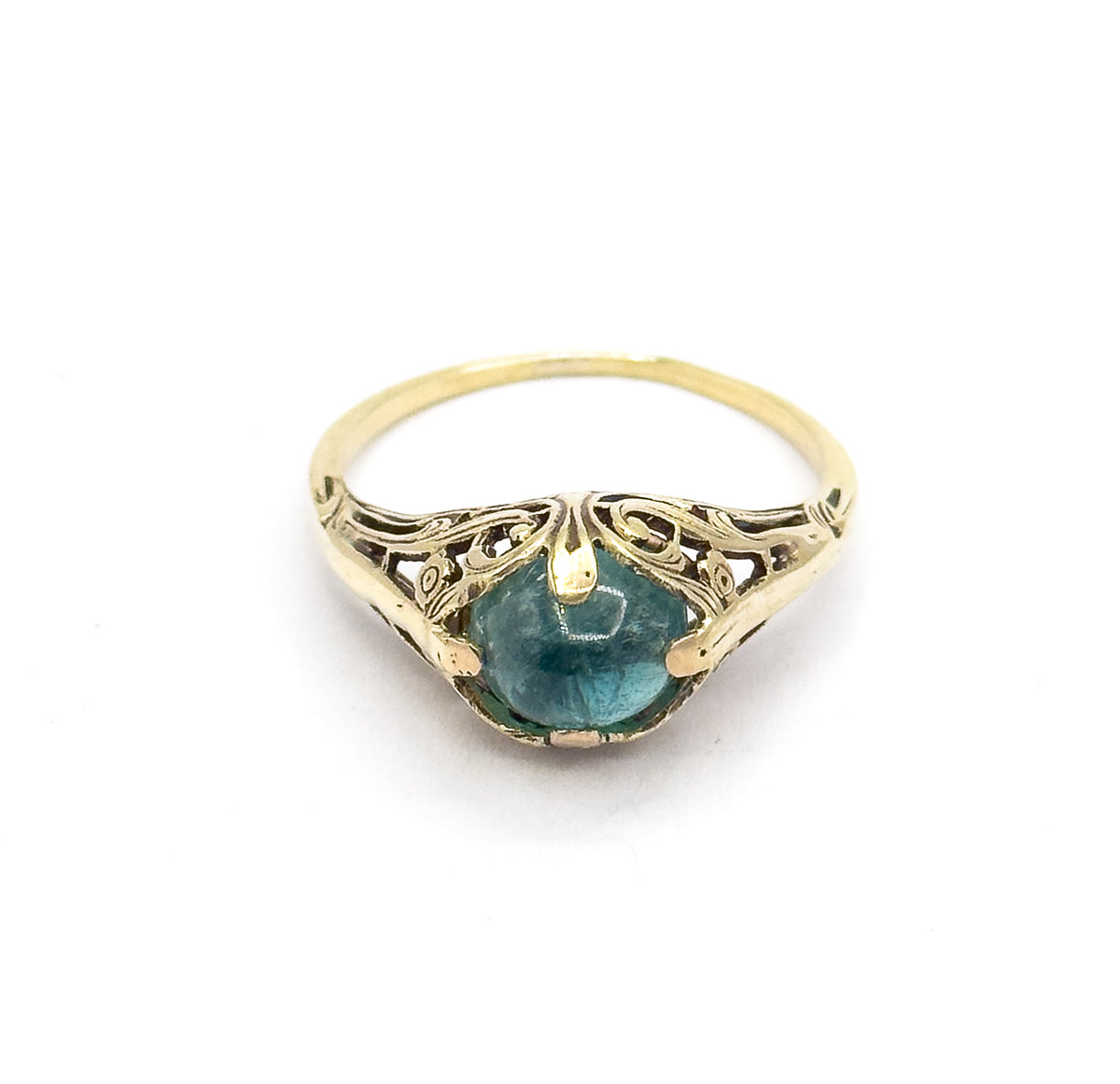 Tilted forward so the ring is seen from the top edge, the greenish blue cabochon sits low between prongs beneath the arching pierced fern gallery and slender split shank.